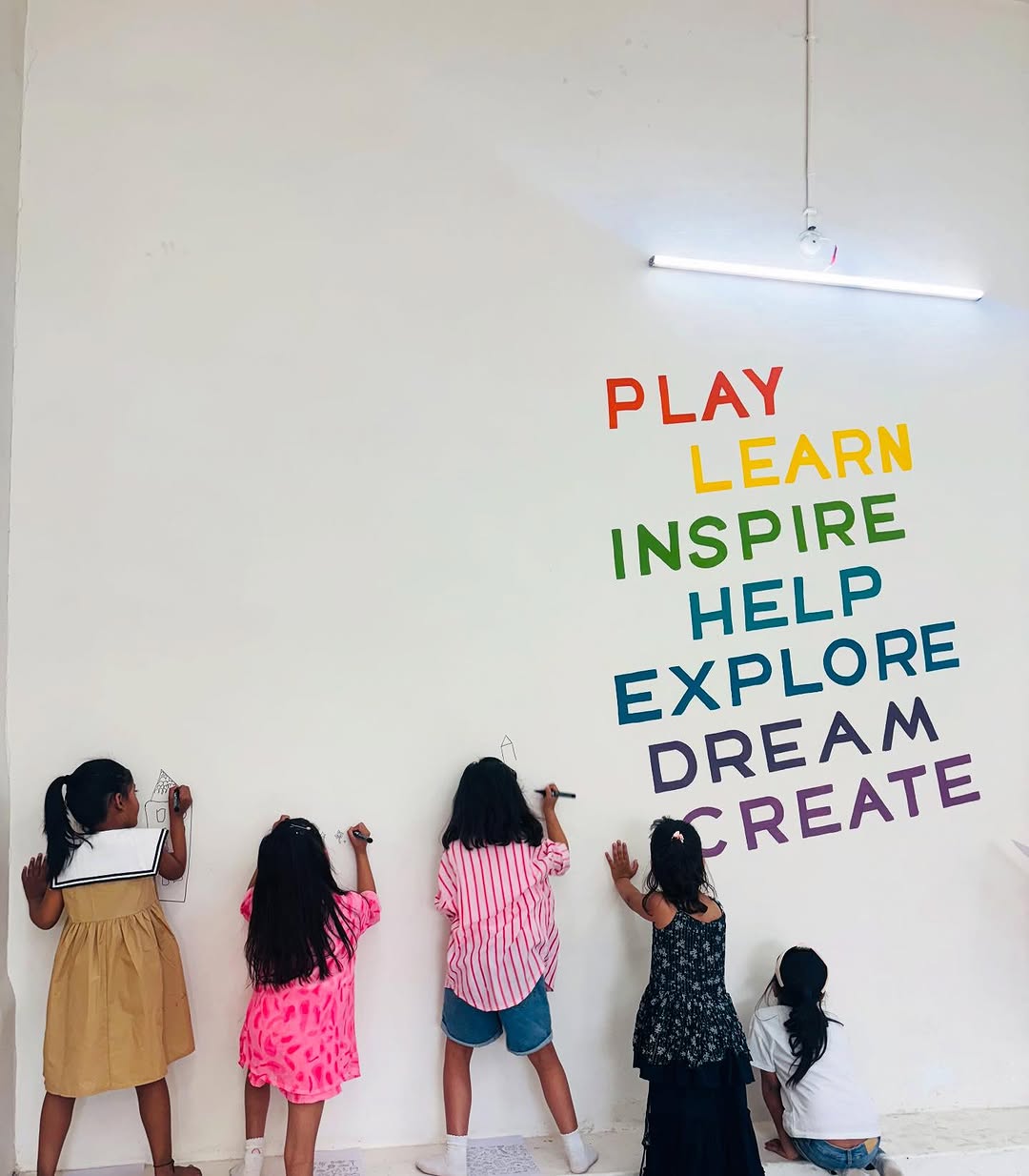 Five children drawing on the wall beside the painted words play, learn, inspire, help, explore, dream, create