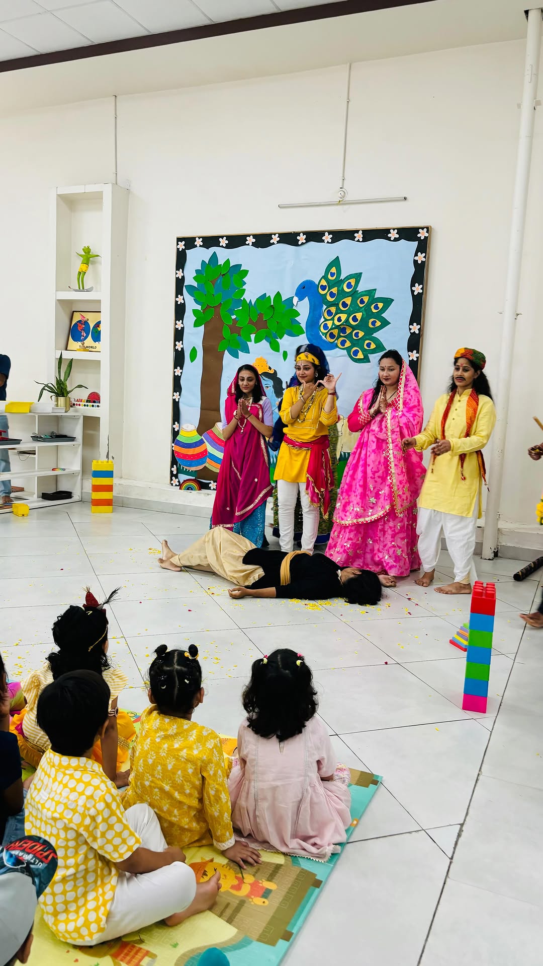 Teachers in traditional dress performing a festival play for the children, who watch from a mat on the floor